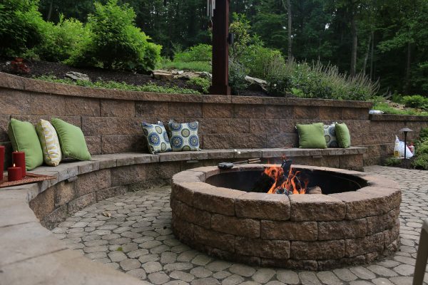 Retaining wall block with fireplace and stone benches with pillows in a forest